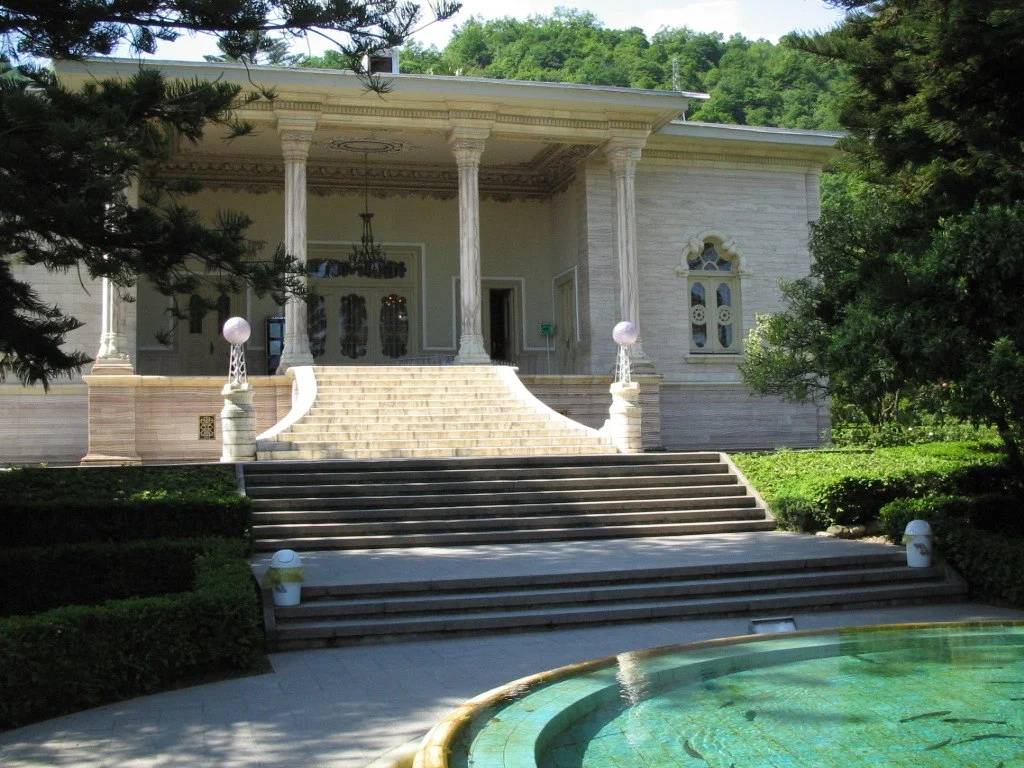 عمارت مرمری رامسر با ستون‌های سنگی و حوض مقابل آن در دل باغ سرسبز